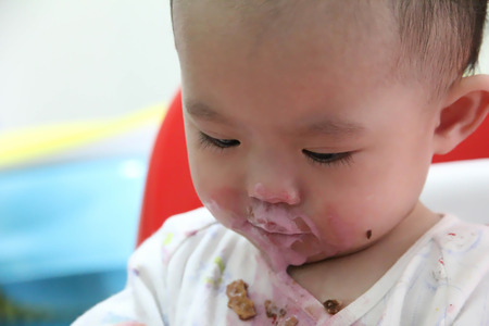Baby on high chair eat ice cream with dirty mouthの写真素材