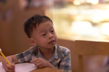 Boy is thinking while writing homework on tableの写真素材