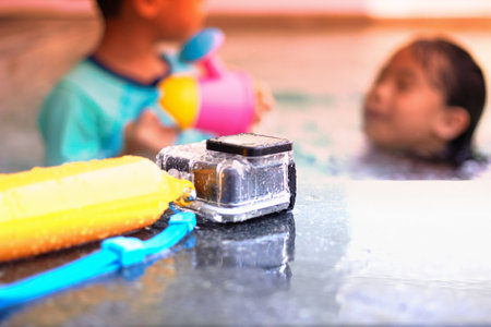 Action camera in waterproof case and floater grip on poolside and blur swimming pool and blur kids...