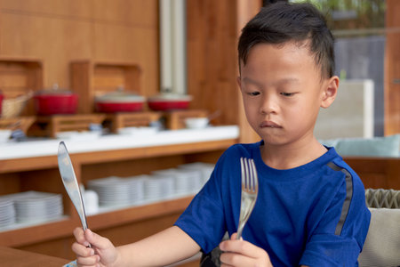 asian boy holds fork and knife prepare eating on table on buffet restaurant backgroundの写真素材