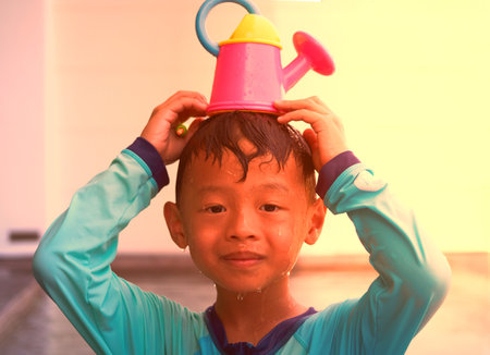 Boy hold water pouring on head with smile face in summer water play vacation holiday concept with sun lightの写真素材