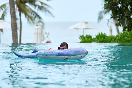 Girl wear goggles on floater in swimming pool with water splash on blur beach backgroundの写真素材