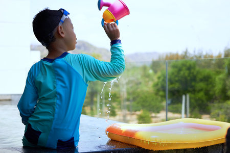 boy plays water pouring on poolside in swimming pool with sun light in summer vacation time