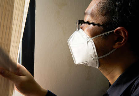 man look outside through window in quarantine period for free living from covid-19 pandermicの写真素材
