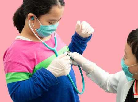asia boy and girl play doctor patient with gown and stethoscope isolated on pink backgroundの写真素材