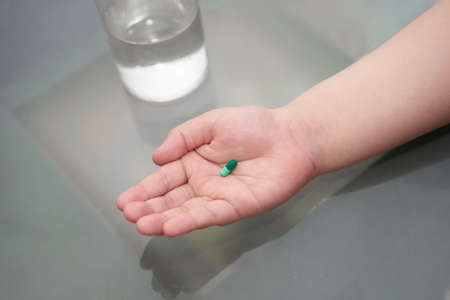 kid hand hold pill supplement antioxidant vitamin mineral capsule with water glass before take...
