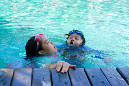 Kids hold on poolsidein swimming suit play and swim in water pool in resortの写真素材