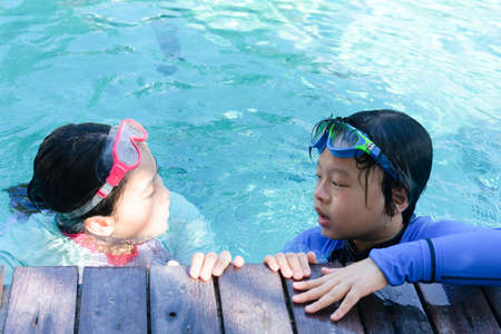 Kids hold on poolsidein swimming suit play and swim in water pool in resortの写真素材