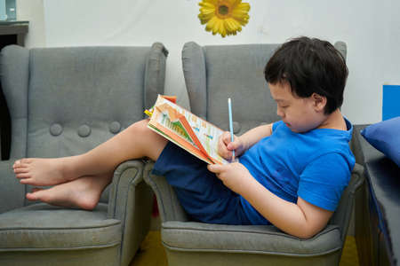 Asian boy sitting on sofa with homework book and use a pencil to do the assigned homework at homeÂ の写真素材