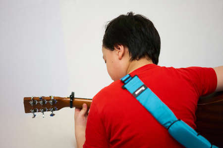 photo from behind black haired boy playing guitar with chords and capo and has a sash sitting in the...