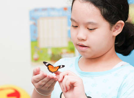 A girl holding up a finger with a butterfly on it. in the living room in the houseの写真素材