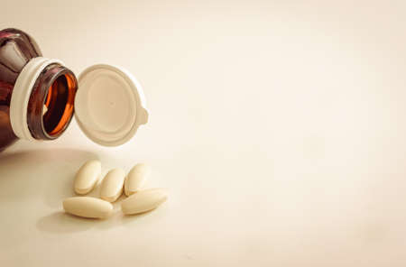medicine pill tablets spill from medical bottle container on floor in abuse or health vitamins supplement conceptの写真素材