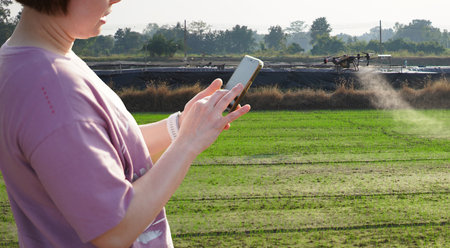 Woman using a mobile phone in a farm, surrounded by farm, control Agriculture Petrol Drone Sprayer .の写真素材