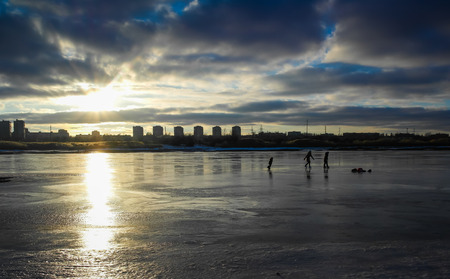 The children play on the skate on the ice Bay at sunset against the backdrop of the cityの写真素材