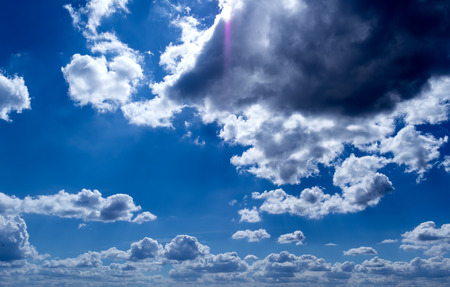 the rays of the Sun, and white and dark Cumulus clouds on a blue skyの写真素材