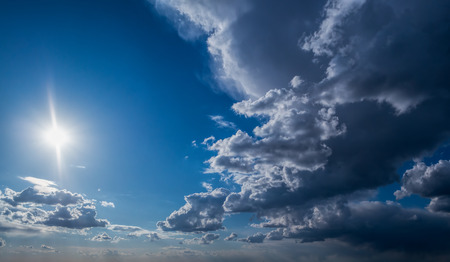 Sun and White and dark Cumulus clouds on a blue skyの写真素材