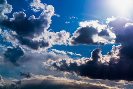 Sun and White and dark Cumulus clouds on a blue skyの写真素材