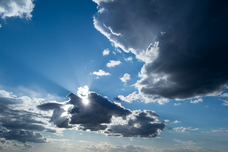 the rays of the Sun, and white and dark Cumulus clouds on a blue skyの写真素材