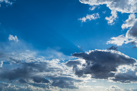 the rays of the Sun, and white and dark Cumulus clouds on a blue skyの写真素材