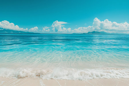 Clear turquoise sea under a vast blue sky, with distant mountains and soft sandy shore.の素材