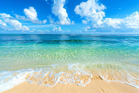 Clear turquoise water meets a sandy beach under a blue sky with fluffy clouds.の素材