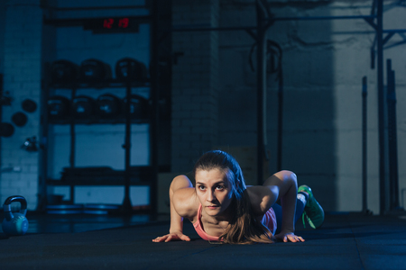 Fit woman in colourful sportswear doing burpees on a exercise mat in a grungy industrial type spaceの写真素材