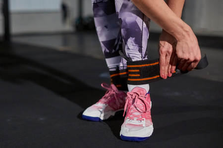 Beautiful girl in a gym on a background of a concrete wall fastens a leg on an elastic bandage. Cross fitの写真素材