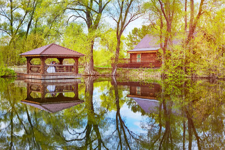 The bride and groom stand in a wooden gazebo on the lake. Spring trees are reflected in the waterの写真素材