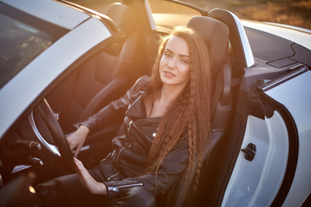 beautiful sexy girl with long hair in a leather jacket and leather pants in sunglasses sits in a...