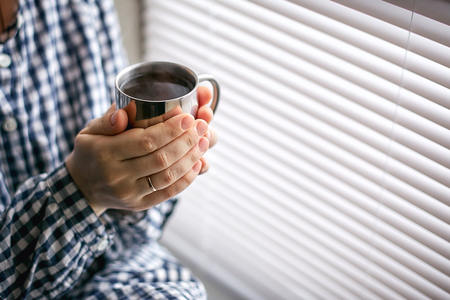 a young woman sits by the window and holds a mug with hot teaの写真素材