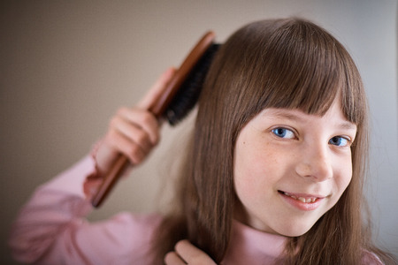 little girl with freckles and blue eyes combing her hairの写真素材