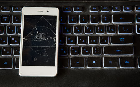 smartphone with broken screen on the background of the old backlit computer keyboardの写真素材