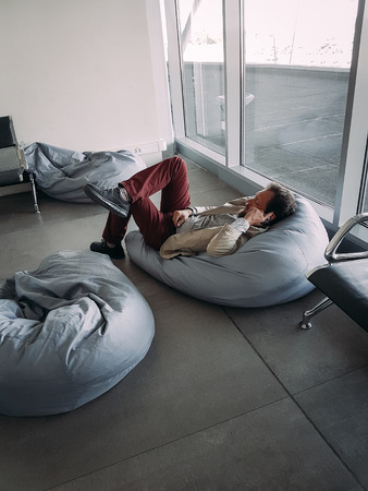 Caucasian businessman with a beard waiting for his flight at the airport and talking on the phone lying downの写真素材