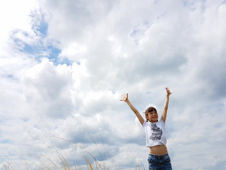 a girl in a white t-shirt runs through the hills on a summer day against the sky.の写真素材