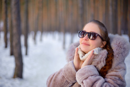 Beautiful womanin winter forest wearing a fur coat and sunglasses. It is snowing. She is happy in winter. Smiling. Winter park. Winter forest.の写真素材