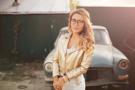 a beautiful blonde with long hair in white denim shorts stands near an old retro car