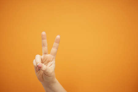 female hand shows victory sign on orange background