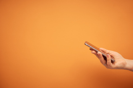 communication. woman hand holding smartphone on orange backgroundの写真素材