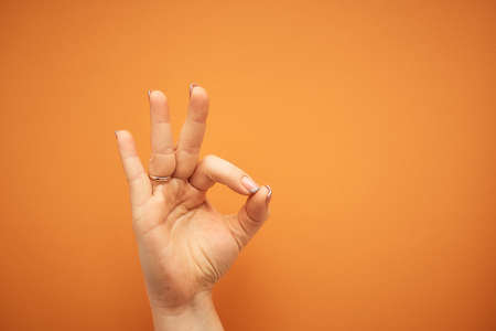gesture, female hand shows OK sign isolated on orange background