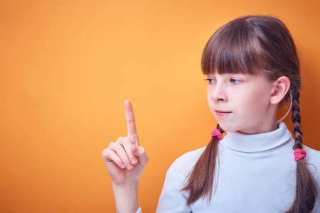 conceptual idea, Caucasian teen girl shows index finger up on colored background, place for textの写真素材