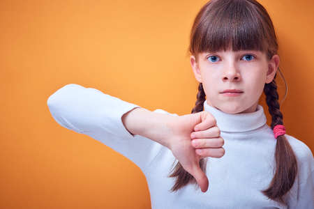 disagreement and protest, Caucasian teen girl shows thumb down on colored background, place for text
