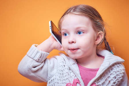 little Caucasian girl with a phone in her hand on a colored background, a place for textの写真素材
