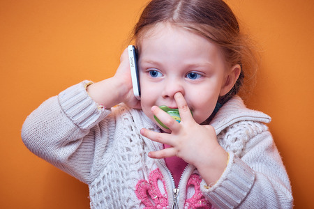 little Caucasian girl with a phone in her hand on a colored background, a place for textの写真素材