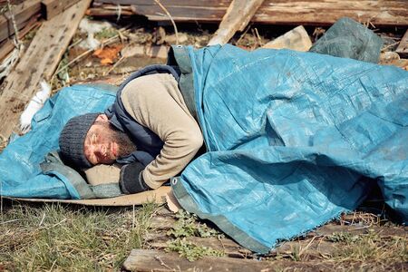 a homeless man near the ruins sleeps on cardboard boxes, helping poor and hungry people during the epidemicの写真素材