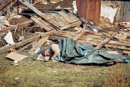 a homeless man near the ruins sleeps on cardboard boxes, helping poor and hungry people during the epidemicの写真素材