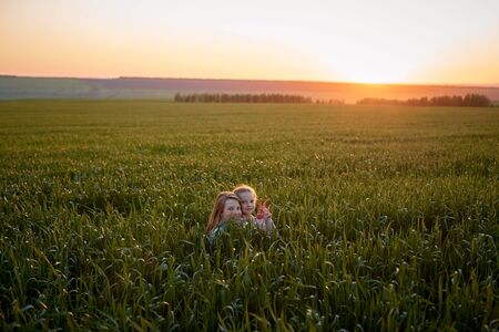two sisters sit in the long grass at sunset, the girls play hide-and-seekの写真素材