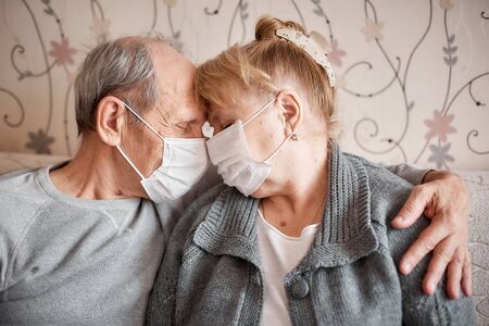 elderly couple in love in medical masks at home in quarantine, family valuesの写真素材