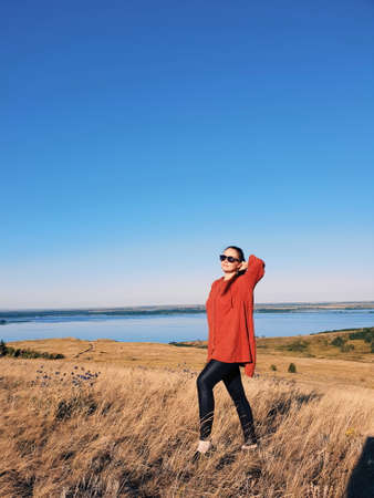 portrait of a woman with sunglasses and red hair in an orange hoodie in a field at sunsetの写真素材