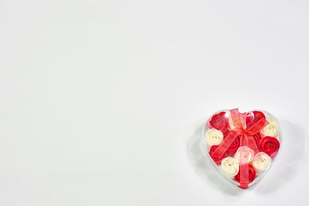 transparent gift box with a ribbon in the shape of a heart with small flowers on a white background, copying space. Valentines Day concept for design.の写真素材