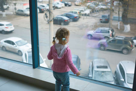 a little girl runs around the new large apartment near a panoramic windowの写真素材